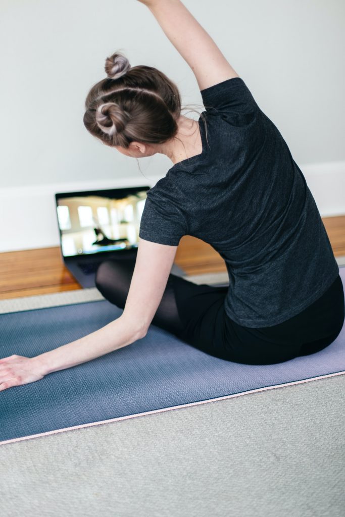 Young woman performing simple yoga move in front of laptop following an online class